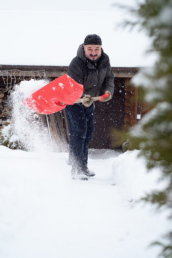 A man cleans the snow at the dacha in winter. There has been a lot of snow. Snowy winter . An adult man with a shovel works on the street.