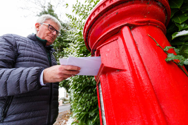 istock Senior man posting a letter in traditional red British mailbox 1448588223