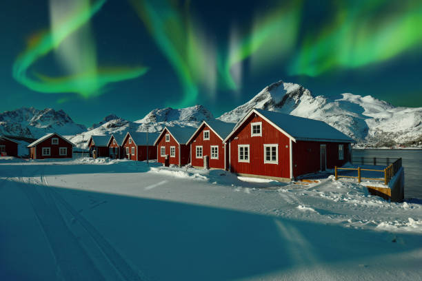 Astonishing winter scenery with traditional Norwegian red wooden houses on the shore of Sundstraumen strait at night with northern lights Astonishing winter scenery with traditional Norwegian red wooden houses on the shore of Sundstraumen strait at night with northern lights. Location: Lofoten; Norway, Europe norway aurora borealis aurora polaris fjord stock pictures, royalty-free photos & images