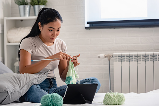 Creative hobbies. Young Asian woman knitting at home. Encouraging neural pathways in brain to stay healthy.