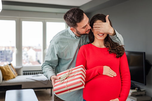 A man is giving a gift to his pregnant wife.