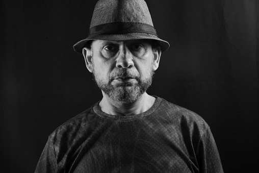 Black and white portrait of a man wearing a hat. Looking at the camera. Isolated on black background.