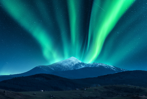 Aurora borealis over the snow covered mountain peak in europe. Northern lights in winter. Night landscape with green polar lights and snowy mountains and hills. Starry sky with aurora. Nature. Space