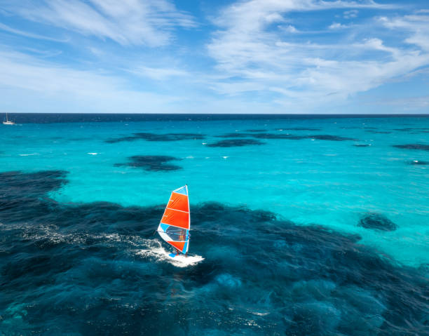 Aerial view of windsurfer on blue sea at sunny summer day. Windsurfing. Extreme sport and vacation. Top view of man on windsurfer board, waves, clear azure water in Sardinia, Italy. Tropical landscape stock photo