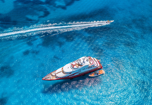 Aerial view of beautiful red luxury yacht and boat in blue sea at sunset in summer. Sardinia island, Italy. Top view of speed boat, sea coast, transparent water. Travel. Tropical landscape. Yachting