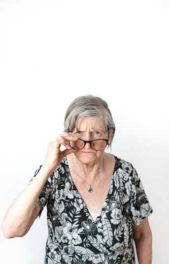 Skeptical woman looking at camera while peering over her eye glasses. White isolated background. Vertical photography with copy space