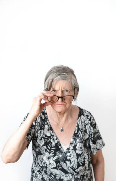 Skeptical woman looking at camera while peering over her eye glasses. White isolated background. stock photo