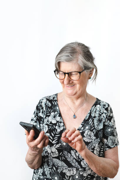 istock Senior lady in her 70's using smart phone and smiling over isolated white background. 1448610530