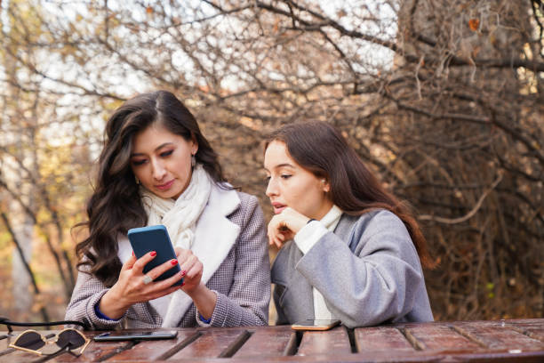 istock two happy young women outdoors looking at cell phone 1448611539