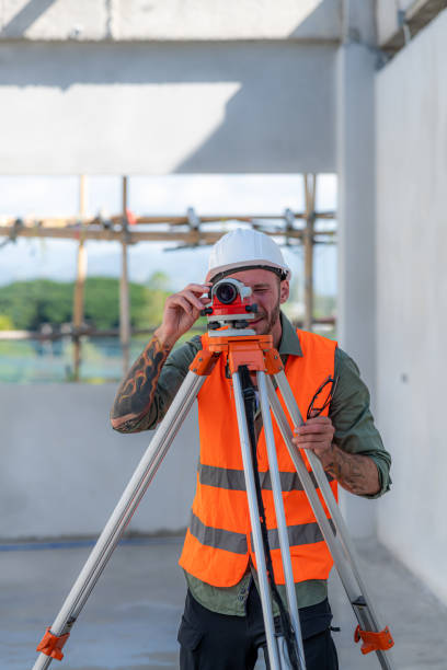 Construction Worker Using Theodolite Surveying Optical Instrument for Measuring Angles in Horizontal and Vertical Planes on Construction Site. Engineer and Architect Using Tablet Next to Surveyor.