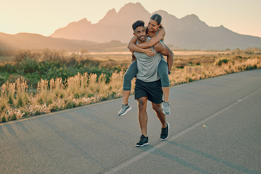 Fitness, exercise and happy couple piggyback outdoors for wellness, training and energy in Cape Town. Young man carrying woman during fun workout in nature, freedom and relax for healthy lifestyle