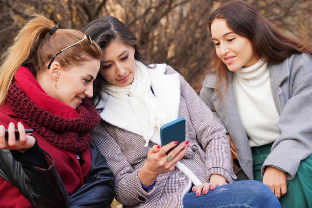 istock Three happy young women outdoors looking at cell phone 1448615471