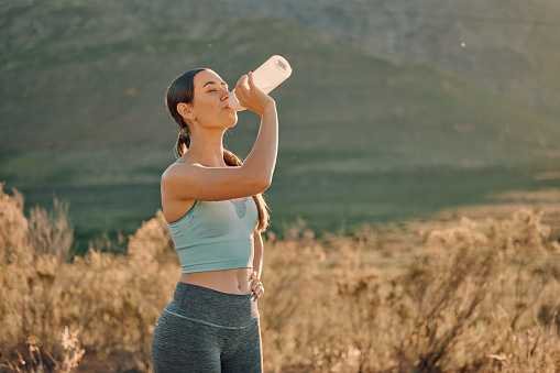 Fitness, exercise and woman drinking water in nature for wellness, hydration and healthy lifestyle. Sports, nutrition and female athlete with water bottle after running, marathon training and workout