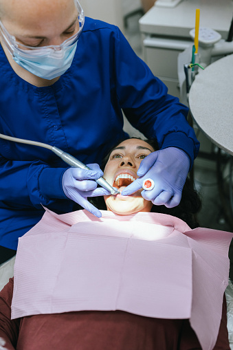 High angle view looking down at a female patient lying in a reclining dentist's chair while her female dentist examines and cleans her teeth.