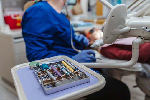 Cropped shot with selective focus on  sterilized dental equipment used for teeth cleaning arranged on a tray in a dental office while in the background an unrecognizable dentist works on a patient.