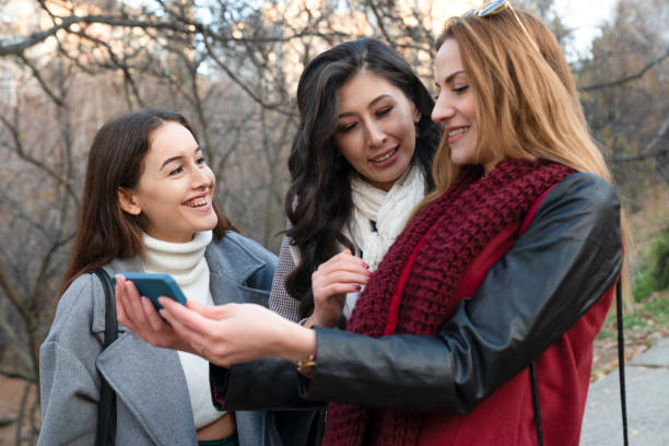 istock Three happy young women outdoors looking at cell phone 1448621119