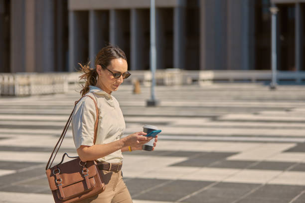 City, smartphone and business woman with coffee for outdoor productivity, 5g networking and email marketing communication. Travel, walking and busy professional using phone or cellphone chat app stock photo