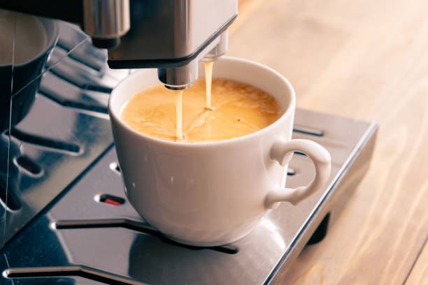 Espresso coffee preparation on a wooden table. Pouring doppio in white cup. Coffee machine on rustic wooden table makes aroma drink. Beautiful foam