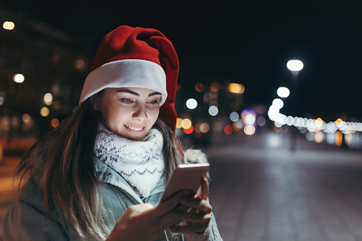 Young women celebrating Christmas alone. She is walking alone and using phone. Happy person positive emotion Holiday concept