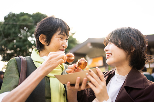 Takoyaki - Japanese junk food from the Kansai region of Japan.
Japanese mother and daughter eating takoyaki outdoors.
Eating standing up.