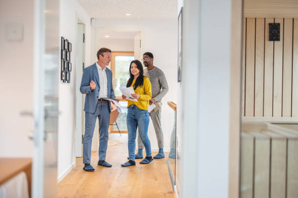 adult caucasian male real estate agent selling and showing the modern apartment to his diverse young clients that are standing next to him in the fancy apartment - investigates imagens e fotografias de stock