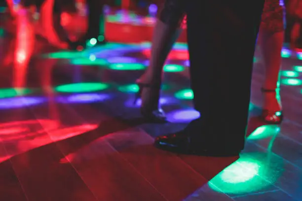 Photo of Dancing shoes of a couple, couples dancing traditional latin argentinian dance milonga in the ballroom, tango salsa bachata kizomba lesson, festival on a wooden floor, purple, red and violet lights