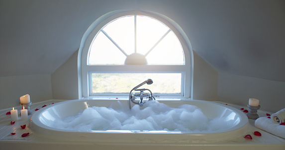 Empty bubble bath, water foam and candles or rose petals in bathroom bathing for relax, rest and hygiene. Relaxation, hospitality or health and wellness at a hotel room, luxury spa and hottub.