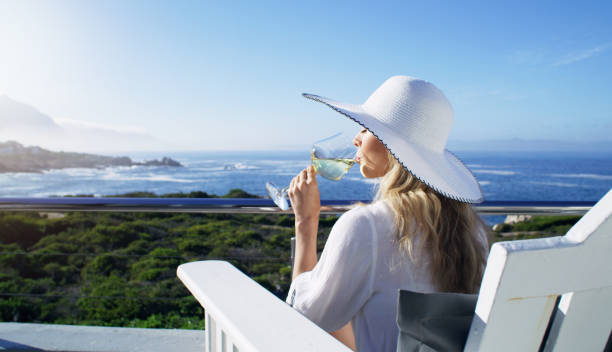 détendez-vous, vin et vacances à l’océan avec une femme en vacances dans un complexe de luxe ou une villa et une belle vue sur la mer et le ciel. nature, eau et alcool avec une jeune femme prenant un verre à l’extérieur - bâtiment vu de lextérieur photos et images de collection