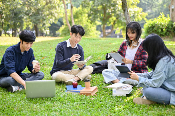 istock Happy young Asian college students relaxing in the campus's park, working their group project 1448654396