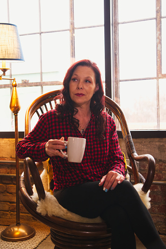 Woman sitting in a chair holding a mug looking away from the camera.