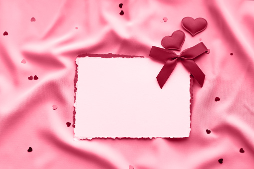 Valentine's day background. Blank white sheet of paper with decorative red hearts on silk fabric. ?olor Viva Magenta. Demonstrating the colors of 2023.