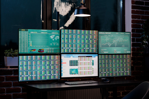 Empty trade office with nobody in it with screens showing financial information and real time data. Interior of forex stock market workstation with multiple display and index charts.