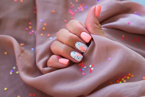 mujeres: una mano con una hermosa manicura sostiene una tela de seda sobre un fondo de destellos. tendencia rosa, puliendo el patrón en las uñas con esmalte de gel, goma laca. día festivo - fingernail manicure beauty decoration fotografías e imágenes de stock