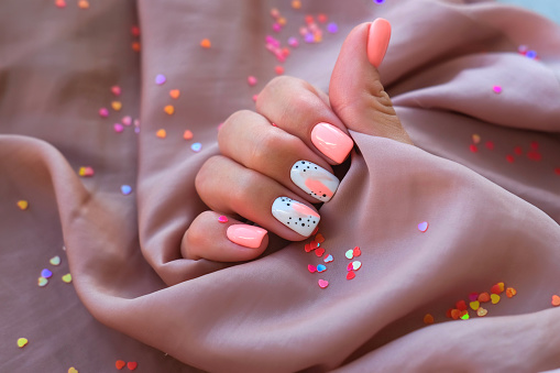 Women - a hand with a beautiful manicure holds a silk fabric on a background of sparkles. Pink trend, polishing the pattern on the nails with gel polish, shellac. Holiday