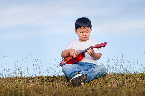 Portrait of Asian child boy playing outdoors. Happy boy with guitar having fun outdoor