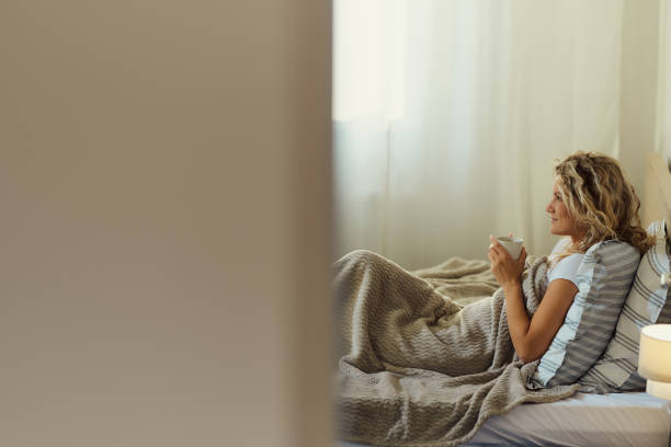 istock Smiling woman day dreaming during morning coffee in bed. 1448683097