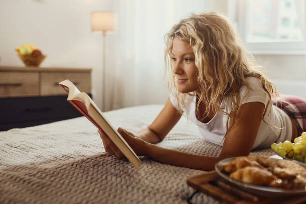 istock Smiling woman reading a book during morning time on a bed. 1448684150