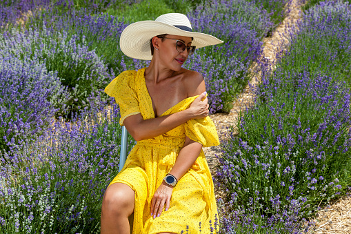 Happy woman near flowering bush lavender. Portrait of young smiling beautiful woman in yellow dress, hat on purple lavender flower blossom meadow field outdoors on summer nature background.