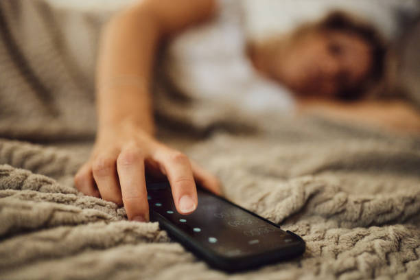 Turning off alarm clock! Close up of unrecognizable woman turning off her alarm clock on cell phone on a bed. alarm clock stock pictures, royalty-free photos & images