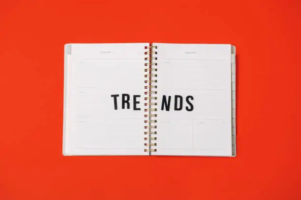 Photo of Global World Trends, Top New trends, forecasting. Word trends in open notepad planner on red background.