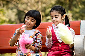 Cute siblings eating cotton candies while sitting in park