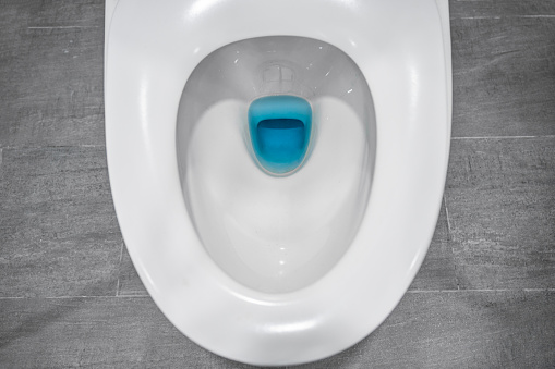 Top view of white toilet flushing bowl with open lid on ceramic gray in the bathroom