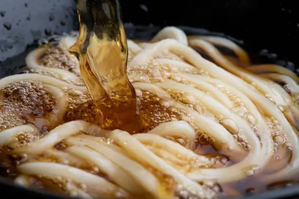 Cooking scene of pour soup stock over udon noodles.