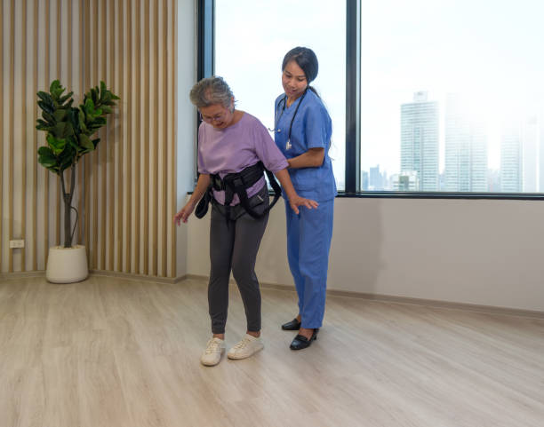 istock Woman physical therapist in blue uniform help an elderly to exercise and practice walking with Safety Transfer Belt. Atmosphere in Community Health Center. 1448698279