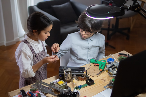 Brother and sister creating technical toy at home. Girl showing necessary elements for robot toy to his brother. Education, hobby and robotics concept