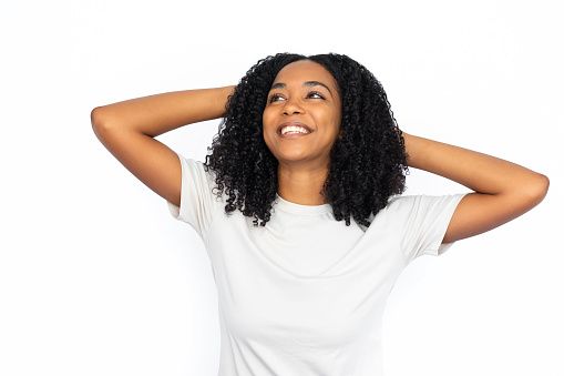 Happy African American woman with hands on head. Portrait of pleased young female model with dark curly hair in white T-shirt looking away, smiling, imagining good things. Success, happiness concept