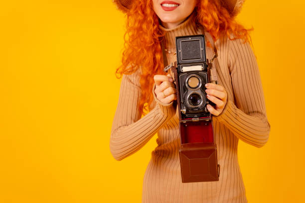 istock Unrecognizable redhead on a yellow background, copy space, with a vintage photo camera 1448705765