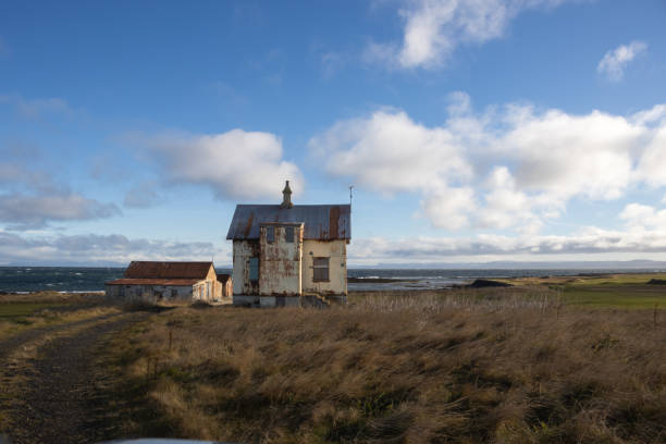 Old abandoned house with a farm. Field close to the Icelandic seaside. Autumn grass. Blue sky with white clouds. Holmsvollur, Sudurnesjabaer, Iceland.