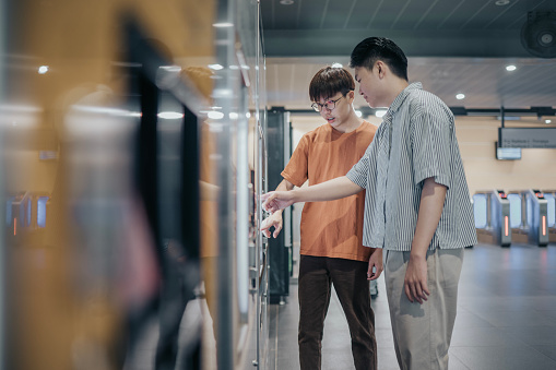 2 Generation Z Asian Chinese Teenage boy buying subway ticket at subway station