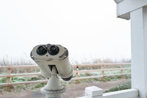 Large seaside binoculars located near a cliff edge overlooking the distant ocean. Heavy fog and ice has made looking through the binoculars impractical.